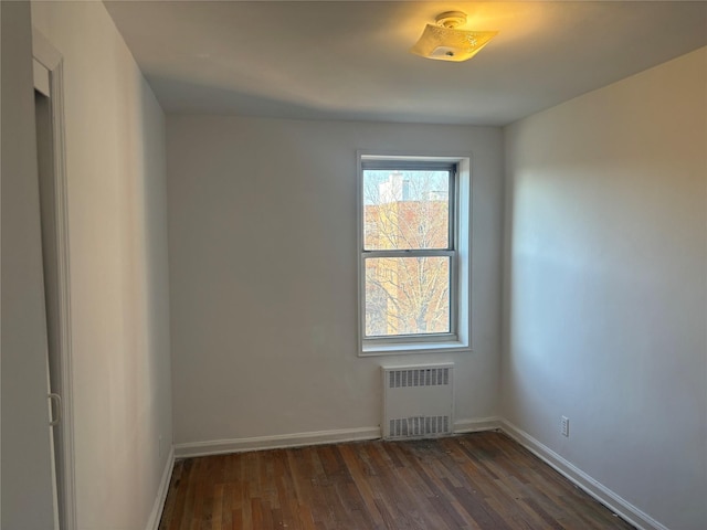 empty room featuring baseboards, dark wood finished floors, and radiator