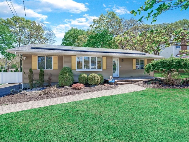 ranch-style home featuring a front lawn, solar panels, and fence