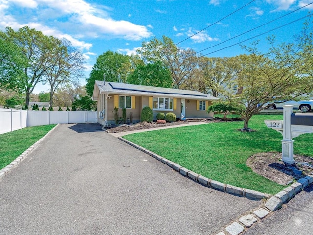 ranch-style house featuring roof mounted solar panels, driveway, fence, and a front yard