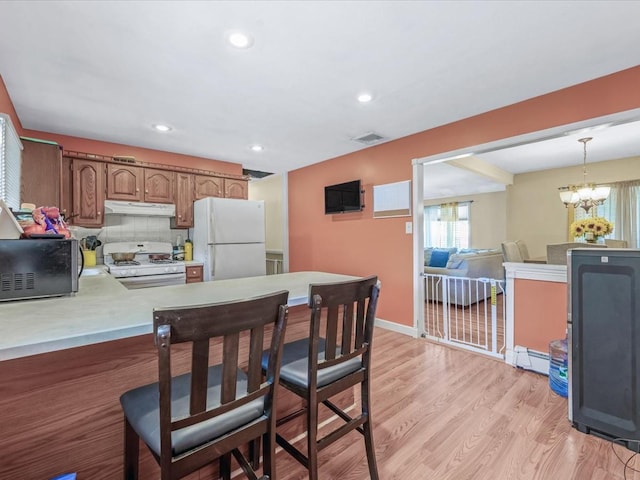 kitchen featuring a peninsula, white appliances, light wood-type flooring, under cabinet range hood, and light countertops