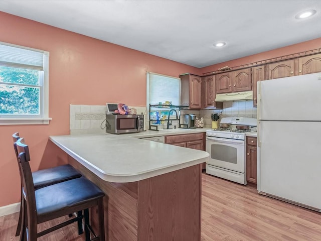 kitchen featuring a sink, a peninsula, white appliances, under cabinet range hood, and light countertops