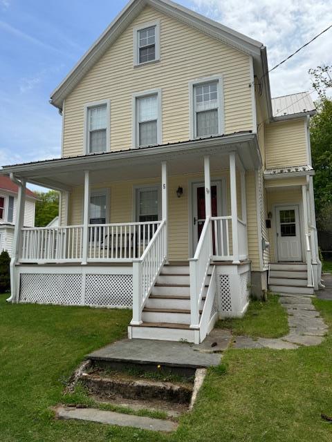 view of front of property featuring covered porch, metal roof, and a front lawn