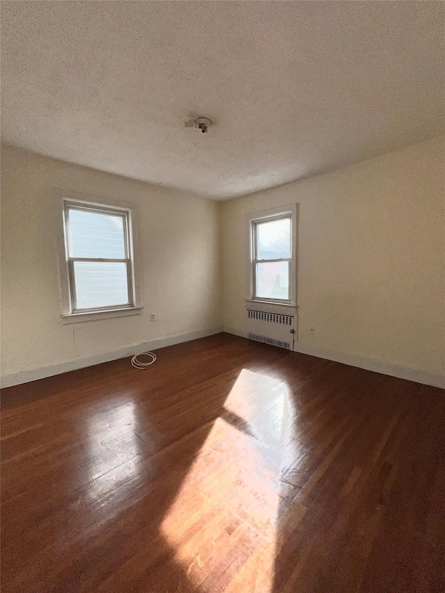 unfurnished room featuring a textured ceiling, baseboards, radiator heating unit, and wood finished floors