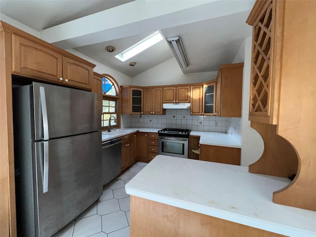 kitchen with appliances with stainless steel finishes, brown cabinetry, under cabinet range hood, vaulted ceiling, and glass insert cabinets