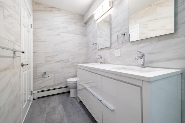 full bathroom with a sink, baseboard heating, double vanity, toilet, and tile walls