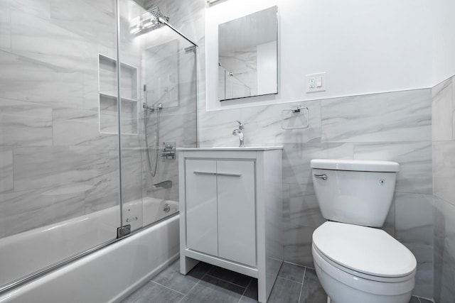 full bath featuring tile walls, tile patterned flooring, vanity, combined bath / shower with glass door, and toilet