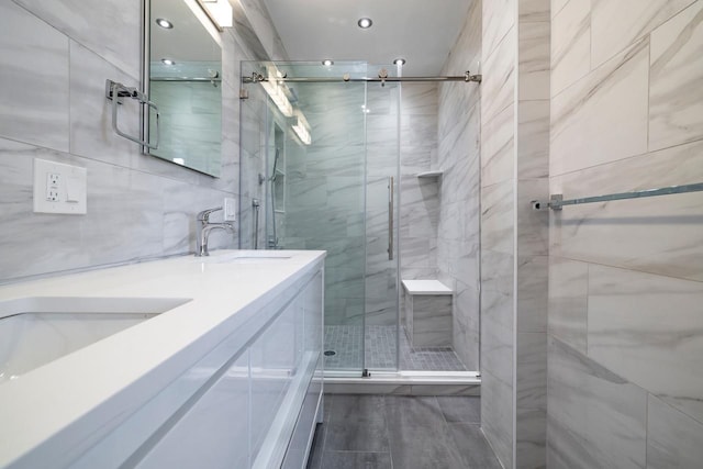 full bathroom with a sink, tile walls, a stall shower, and double vanity