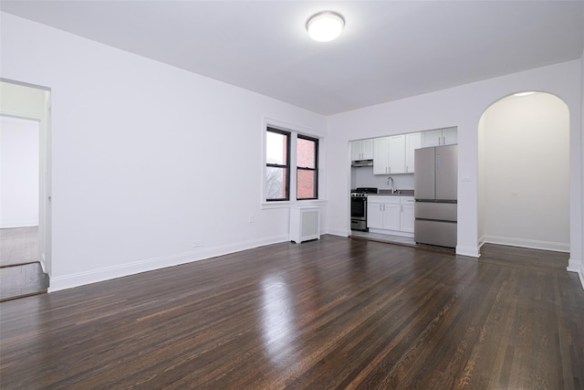 unfurnished living room featuring a sink, arched walkways, baseboards, and dark wood finished floors