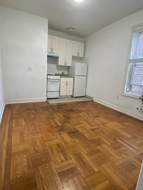 128 W 138th St Unit 5F, New York Manhattan, NY 10030 - kitchen with under cabinet range hood, white appliances, baseboards, and white cabinets