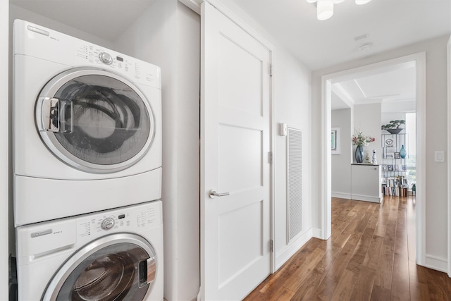 clothes washing area with laundry area, stacked washer and clothes dryer, baseboards, and wood finished floors