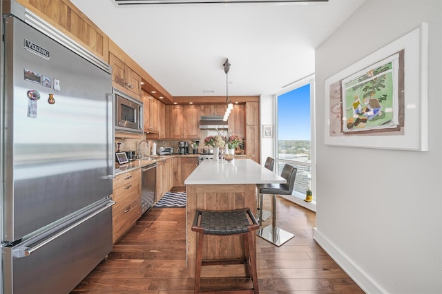 kitchen with a breakfast bar, built in appliances, light countertops, dark wood finished floors, and under cabinet range hood