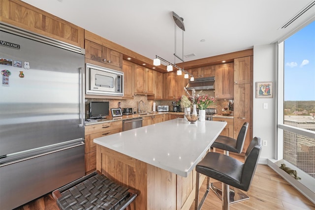 kitchen with decorative backsplash, a sink, built in appliances, under cabinet range hood, and light wood-style flooring