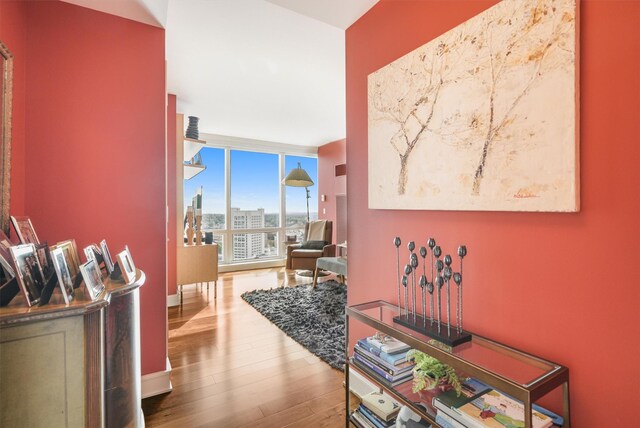 hall featuring baseboards, a city view, floor to ceiling windows, and wood finished floors