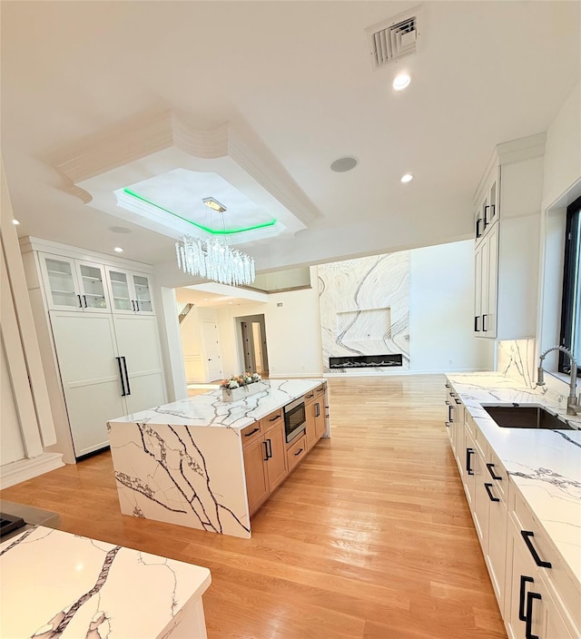 412 Mill River Rd, Oyster Bay, NY 11771 - kitchen with visible vents, glass insert cabinets, stainless steel microwave, a sink, and light wood-style flooring
