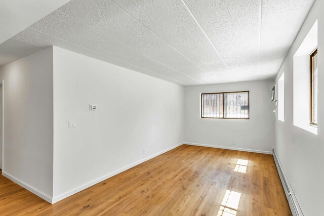 57-15 69th Ln # 2, Maspeth, NY 11378 - spare room featuring a baseboard heating unit, light wood-type flooring, baseboards, and a textured ceiling