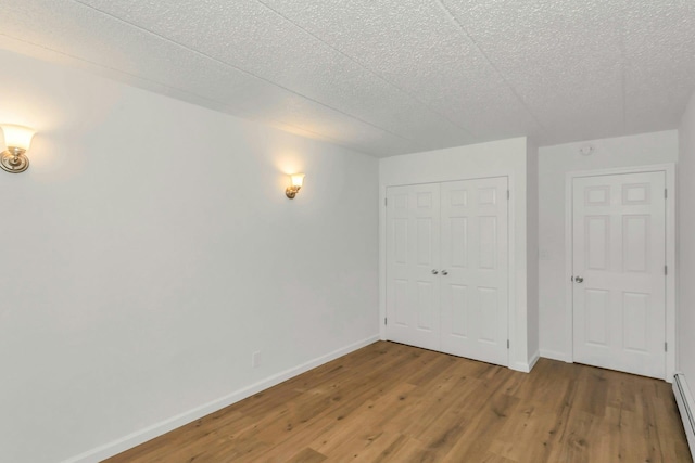 57-15 69th Ln # 2, Maspeth, NY 11378 - unfurnished bedroom featuring wood finished floors, a baseboard radiator, baseboards, a closet, and a textured ceiling