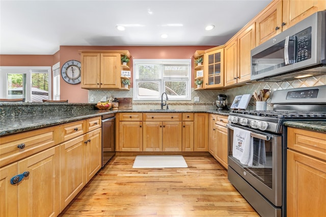 kitchen featuring appliances with stainless steel finishes, light wood-style flooring, a sink, tasteful backsplash, and dark stone countertops