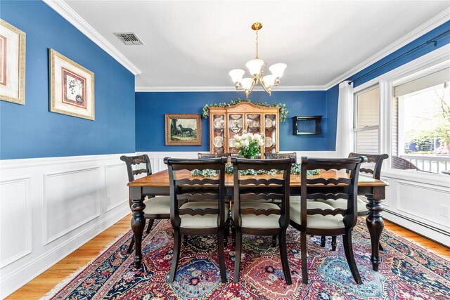 dining area with wood finished floors, ornamental molding, a chandelier, wainscoting, and a decorative wall