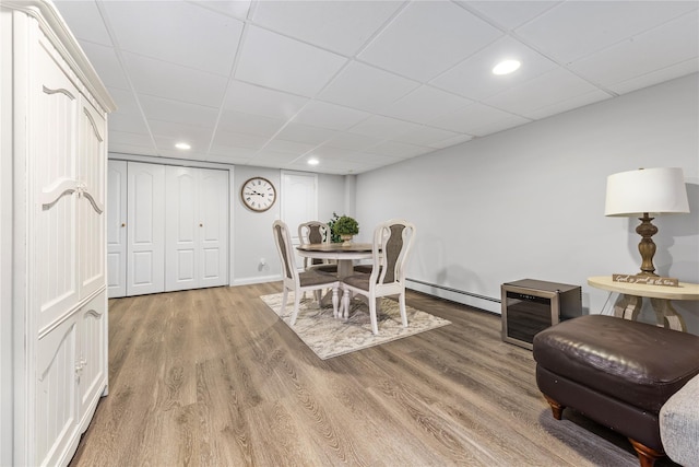 dining room featuring a baseboard heating unit, light wood-style floors, recessed lighting, and a drop ceiling