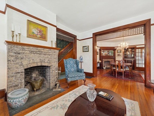 living area with baseboards, an inviting chandelier, hardwood / wood-style flooring, and a fireplace