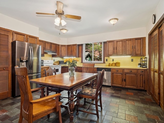 kitchen with under cabinet range hood, light countertops, appliances with stainless steel finishes, and stone tile flooring