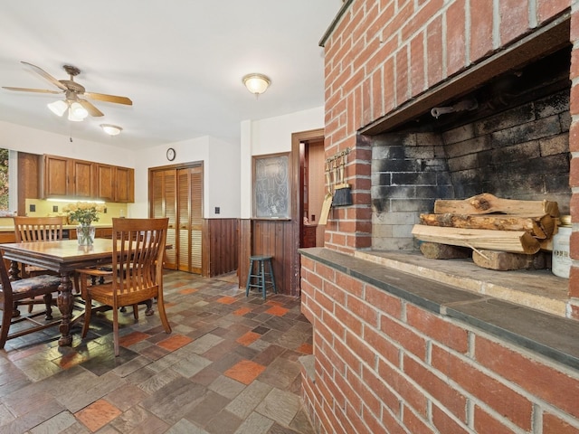 dining area featuring wooden walls, ceiling fan, wainscoting, and stone tile flooring