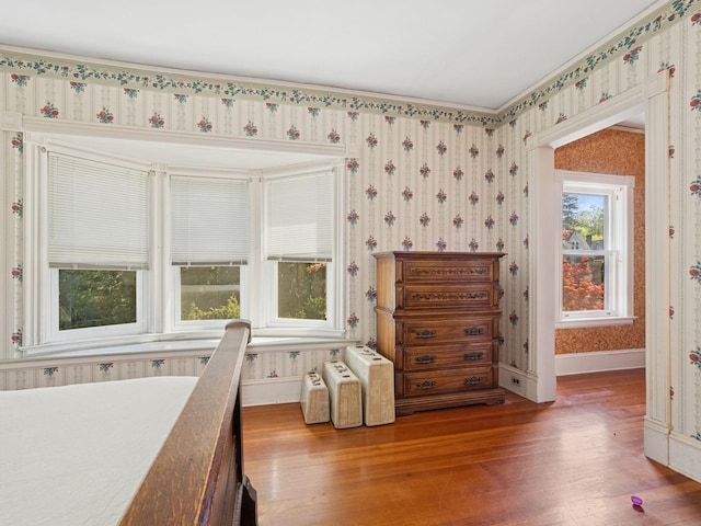 bedroom featuring baseboards, wallpapered walls, and wood finished floors