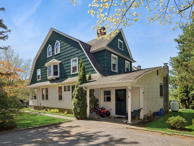 view of front of property with roof with shingles, a chimney, a front yard, and a gambrel roof