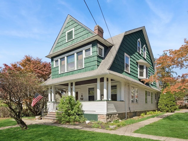 view of front facade featuring a front lawn, a gambrel roof, a chimney, a shingled roof, and a porch