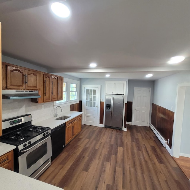 kitchen with a sink, light countertops, a baseboard heating unit, under cabinet range hood, and stainless steel appliances