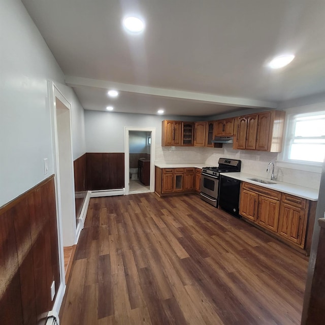 kitchen with stainless steel gas range, light countertops, under cabinet range hood, a wainscoted wall, and a sink