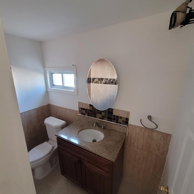 bathroom featuring tile patterned flooring, vanity, toilet, a wainscoted wall, and tile walls