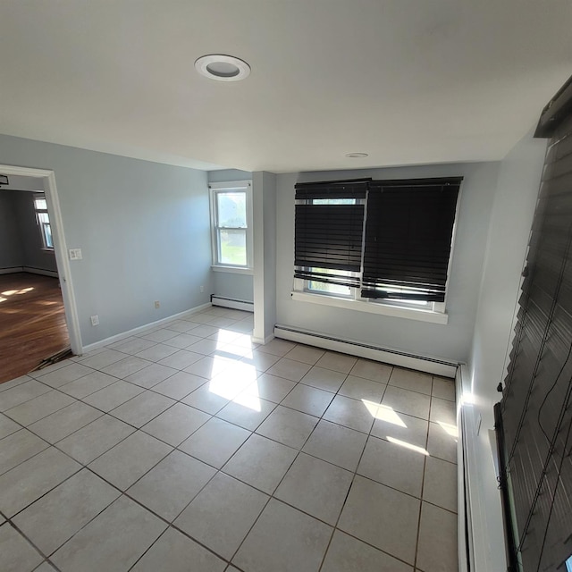 tiled empty room with baseboards, a baseboard radiator, and a wealth of natural light