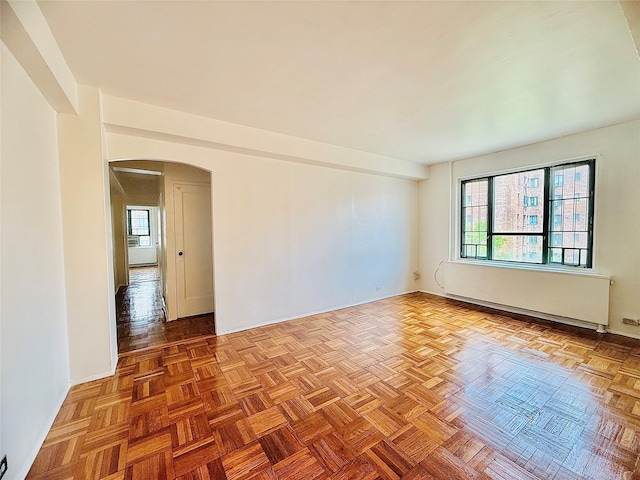 unfurnished room featuring baseboards, arched walkways, and radiator