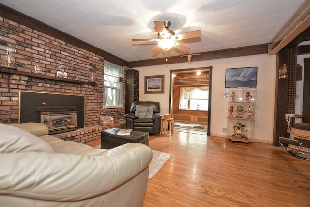 living area with ceiling fan, a brick fireplace, wood finished floors, and baseboards