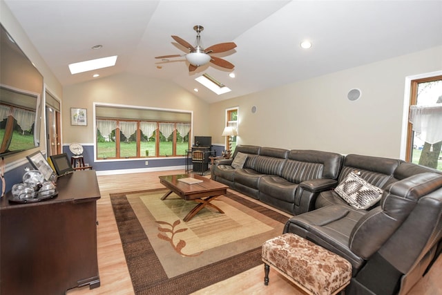 living room featuring a skylight, lofted ceiling, light wood-type flooring, a ceiling fan, and healthy amount of natural light