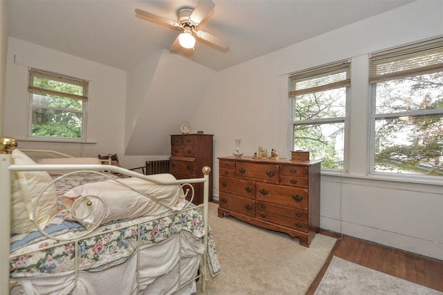 bedroom with multiple windows, vaulted ceiling, radiator heating unit, wood finished floors, and a ceiling fan