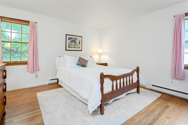 bedroom with a baseboard radiator, light wood-style flooring, and baseboards