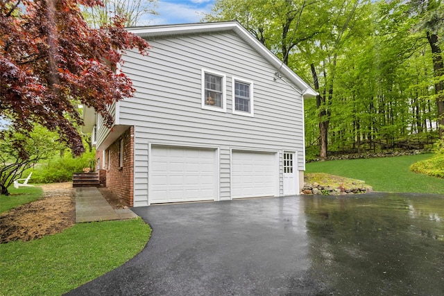 view of property exterior with an attached garage, brick siding, a lawn, and aphalt driveway