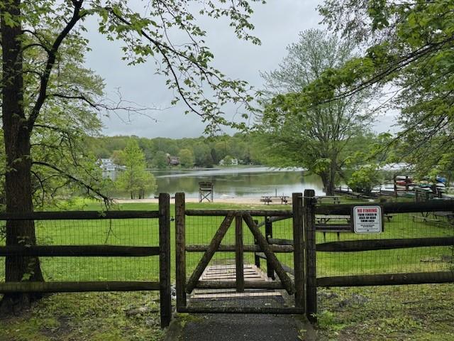 view of gate with a water view, fence, and a lawn