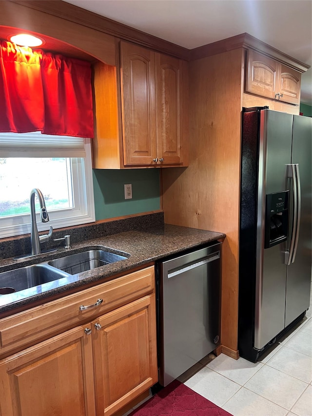 kitchen featuring brown cabinets, appliances with stainless steel finishes, a sink, dark stone countertops, and light tile patterned floors