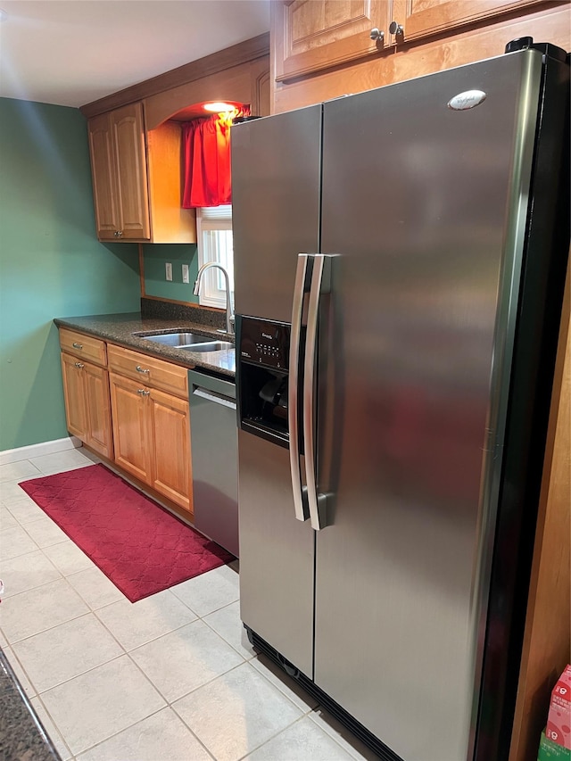 kitchen featuring appliances with stainless steel finishes, a sink, dark stone countertops, baseboards, and light tile patterned floors