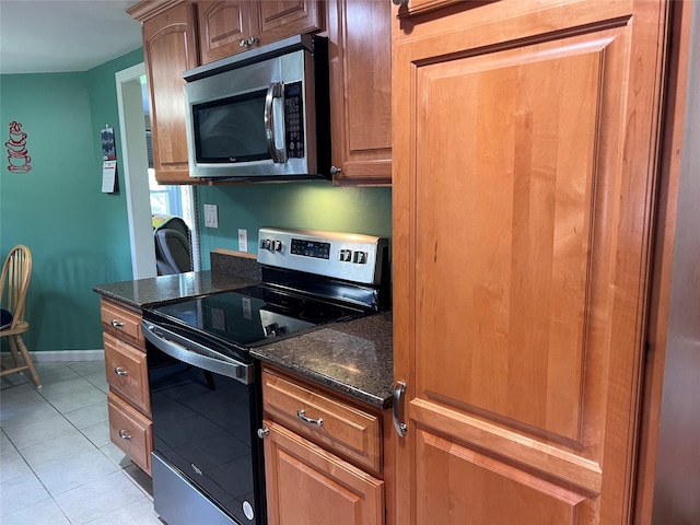 kitchen featuring baseboards, dark stone counters, light tile patterned floors, and stainless steel appliances