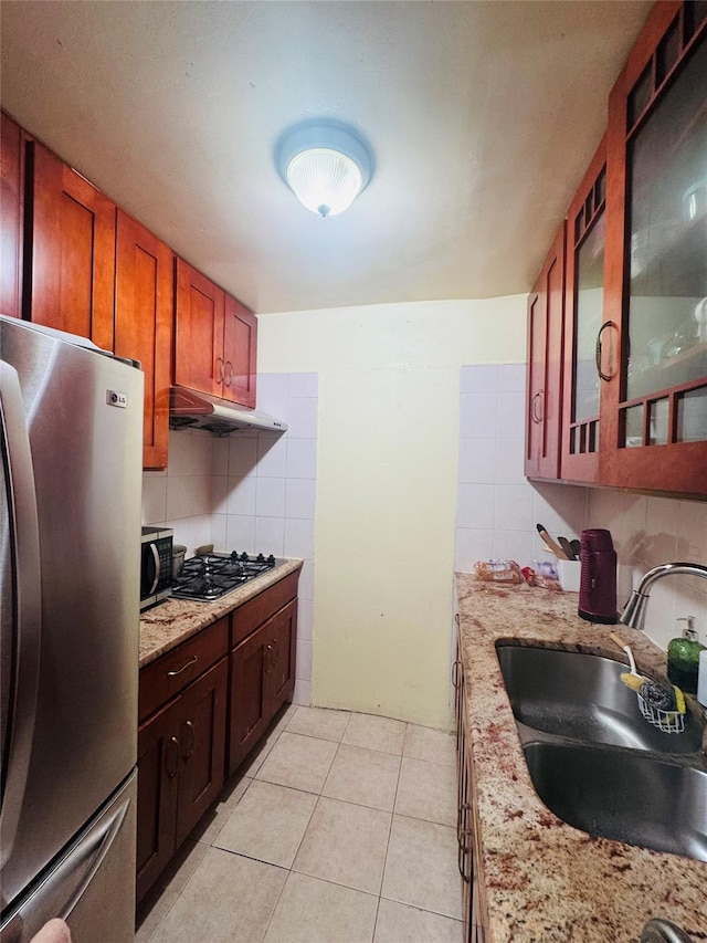 kitchen featuring decorative backsplash, glass insert cabinets, under cabinet range hood, a sink, and stainless steel appliances