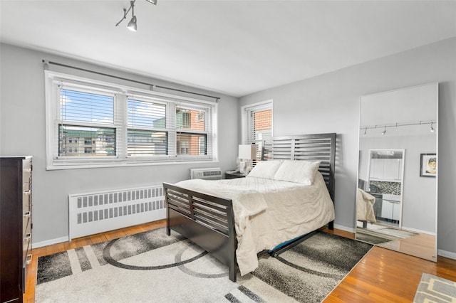 bedroom with rail lighting, wood finished floors, baseboards, and radiator heating unit