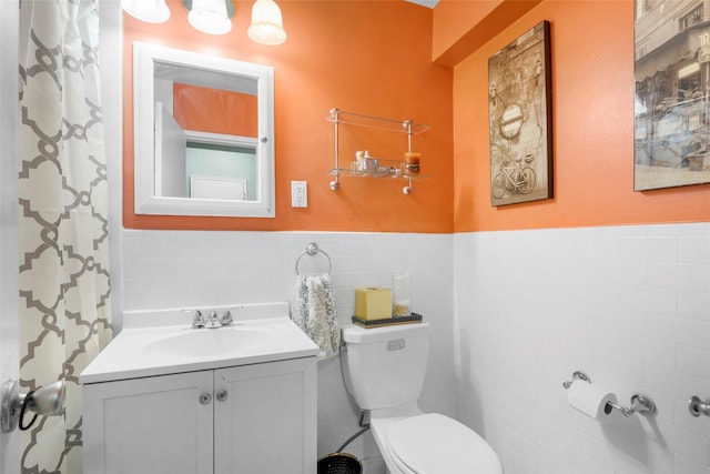 bathroom featuring tile walls, toilet, vanity, and a wainscoted wall