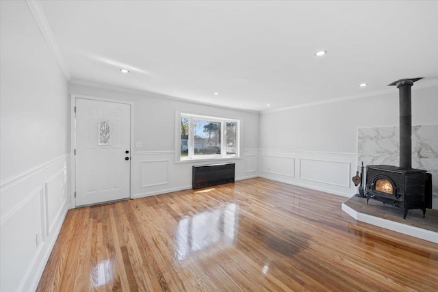 unfurnished living room with a wood stove, ornamental molding, a decorative wall, and radiator heating unit