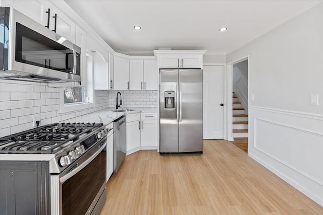 kitchen featuring light wood-style flooring, a sink, white cabinetry, backsplash, and stainless steel appliances