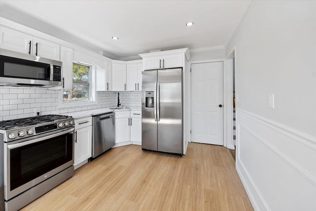 kitchen with a sink, ornamental molding, white cabinetry, light countertops, and appliances with stainless steel finishes