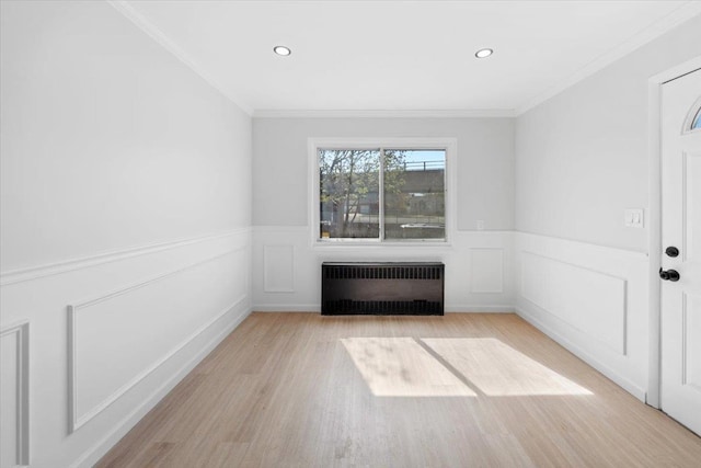 spare room featuring radiator, a wainscoted wall, light wood-style flooring, and ornamental molding